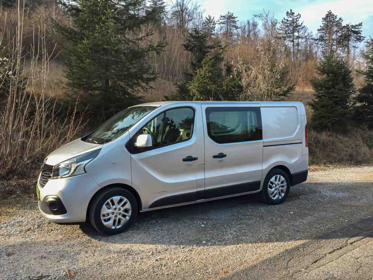 General view of a silver model of the Renault Trafic camper while parked in a wooded area.
