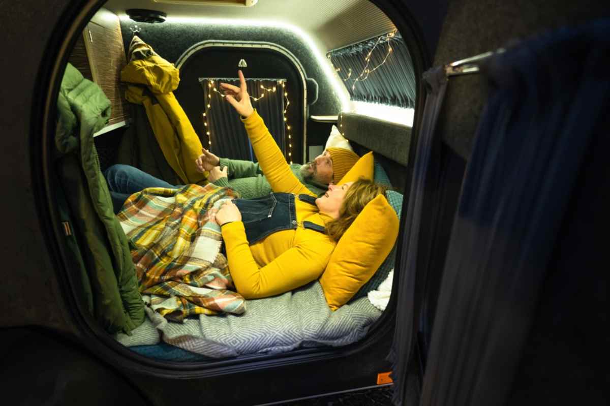 A couple of travelers enjoy the Icelandic night while lying down and staying warm inside their minicamper.