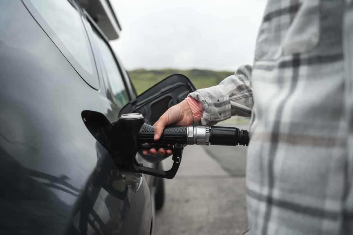 A hand holds a gas pump while inserting it into the gas hole of a vehicle.
