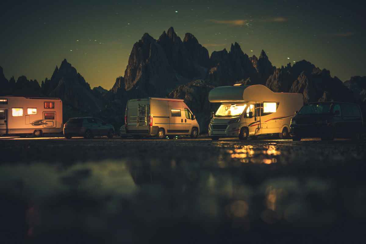 Campers and motorhomes glowing at night under a starry mountain sky.