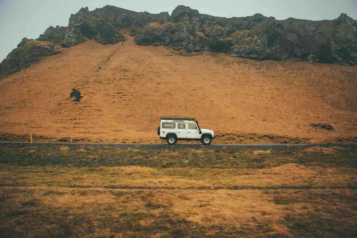 White Land Rover Defender on a paved road below a golden, rocky hillside.