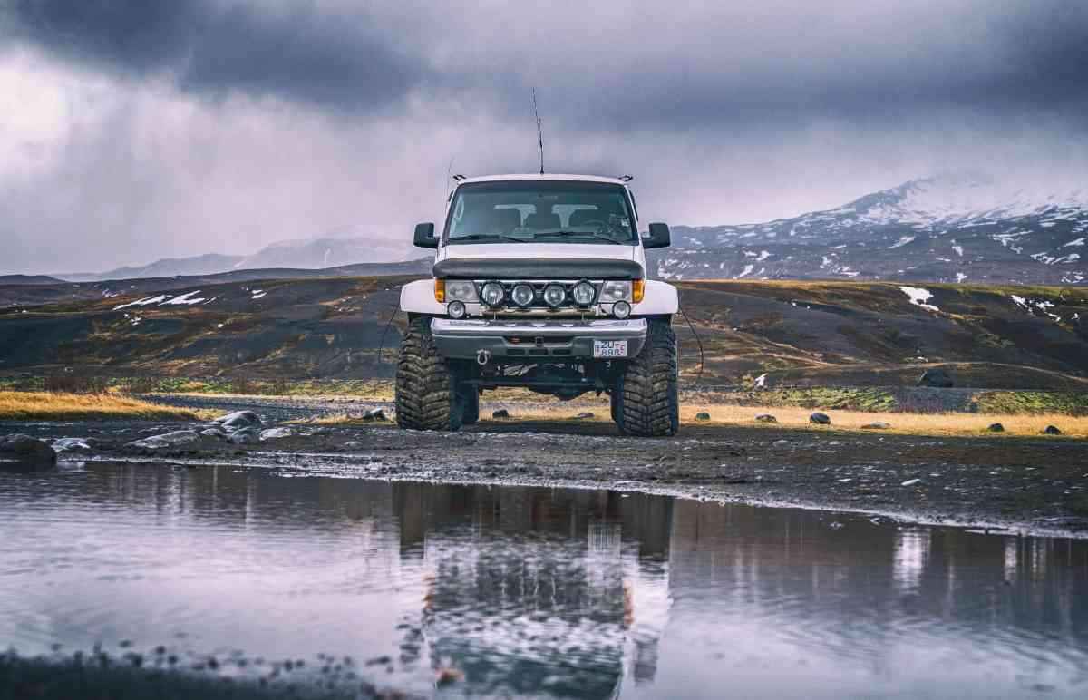 Lifted super-jeep facing the camera with puddle reflections and stormy mountains.