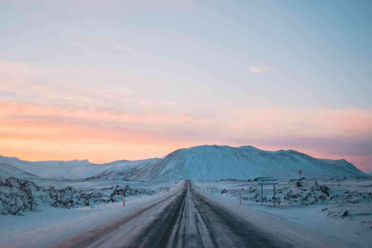 Straight icy road leading to snow-covered peaks at a pastel sunrise in Iceland.