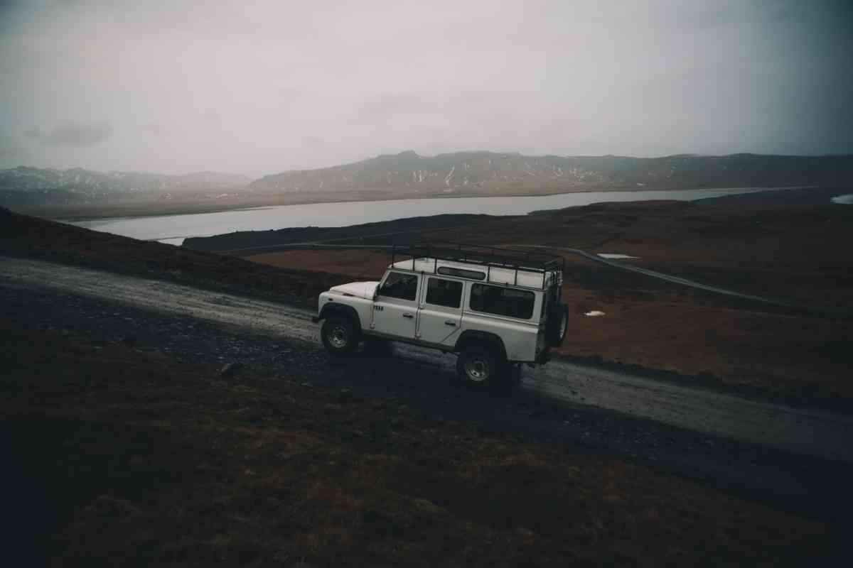 White Land Rover climbing a remote gravel road above a lake on a misty day.