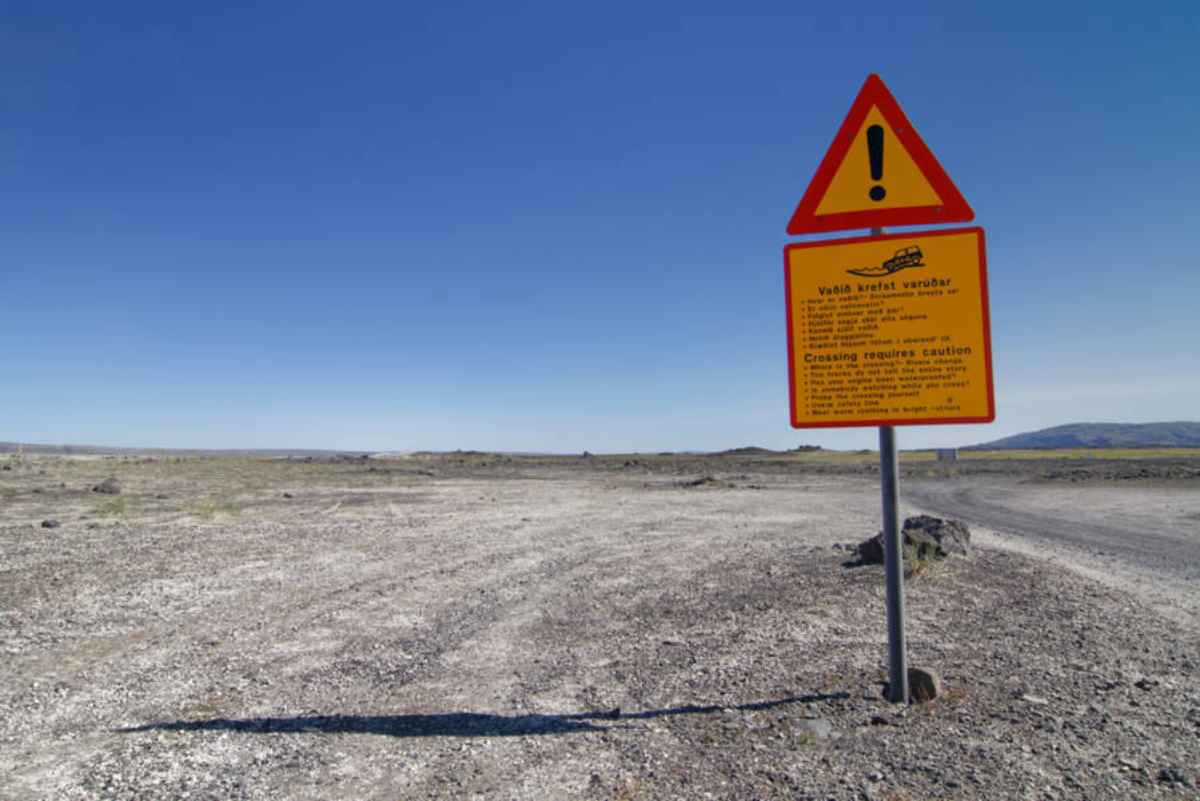 Caution sign about river crossings on Iceland’s F208 Highland road under a clear blue sky.