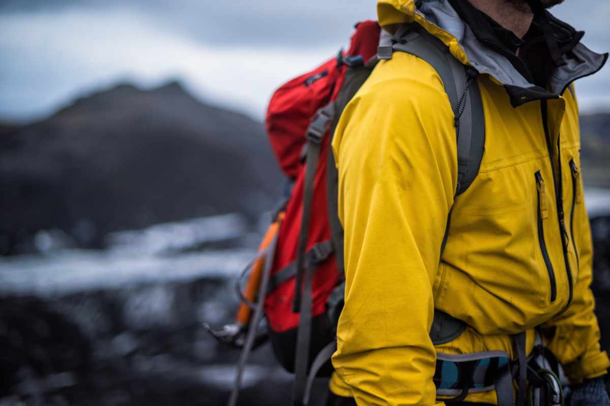 Traveler in a rain shell and poncho near a waterfall, mist swirling all around.