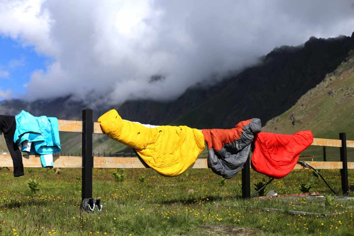 Colorful sleeping bags airing out on a fence in a sunny alpine meadow.