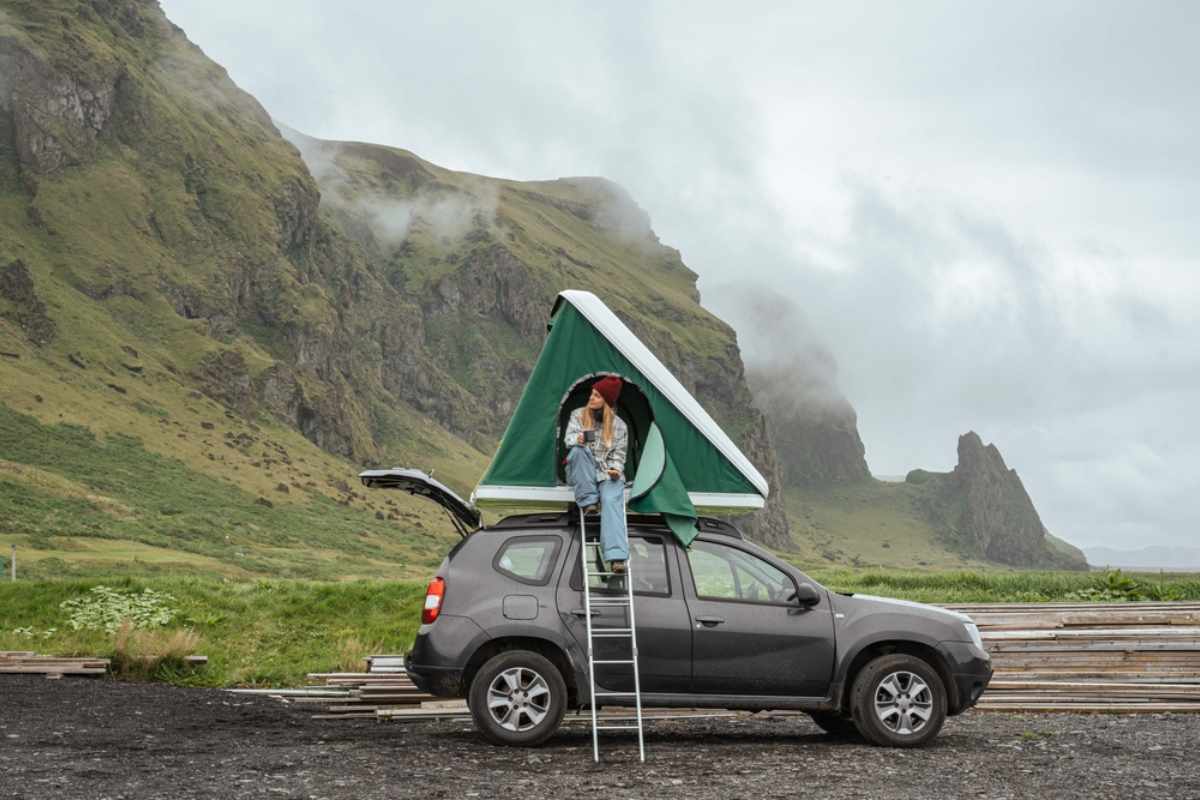 SUV with a roof-top tent; traveler sits at the entrance amid dramatic Icelandic cliffs.