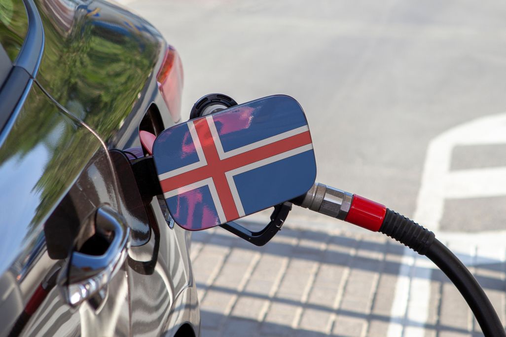 A close-up of a car being refueled at a gas station in Iceland, with the fuel pump showing the Icelandic flag on the nozzle.