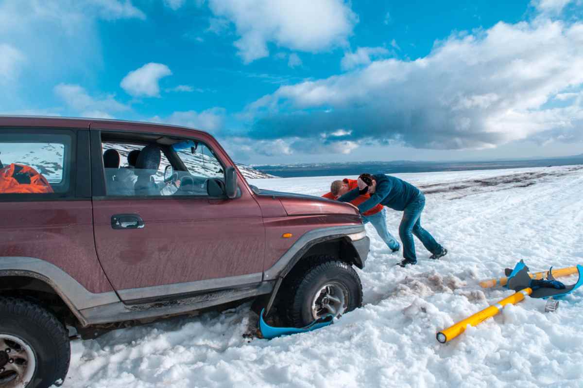 Two men push a 4x4 vehicle that has become stranded on the Icelandic road due to thick snow on the road.