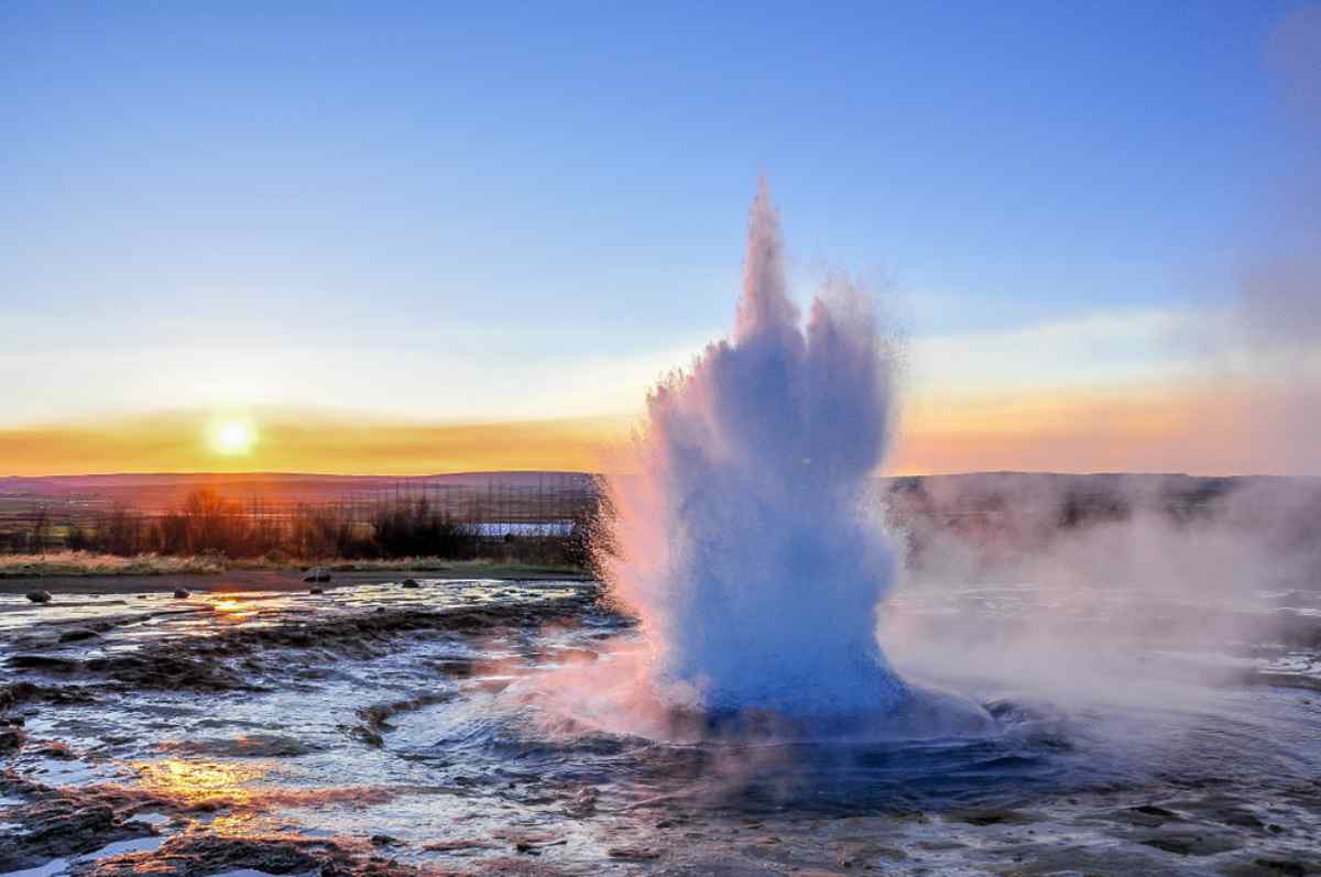 General view of the jet of water emanating from Iceland's Geysir during sunset on what appears to be a frigid day.