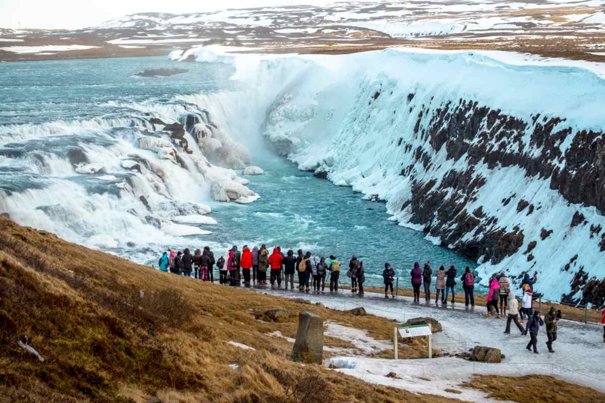 Aerial view of the Gullfoss waterfall in Iceland, completely snowed in, showing a group of tourists watching the waterfall from a designated area.