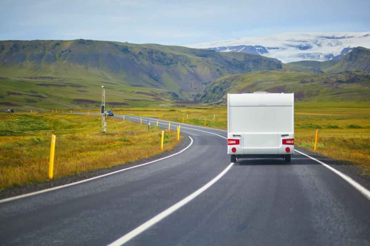 A white RV travels on a winding road through lush green hills under a bright sky, conveying a sense of freedom and adventure.