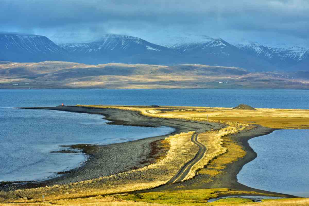 Curving shoreline and causeway in Hvalfjörður fjord with distant snow-dusted mountains.