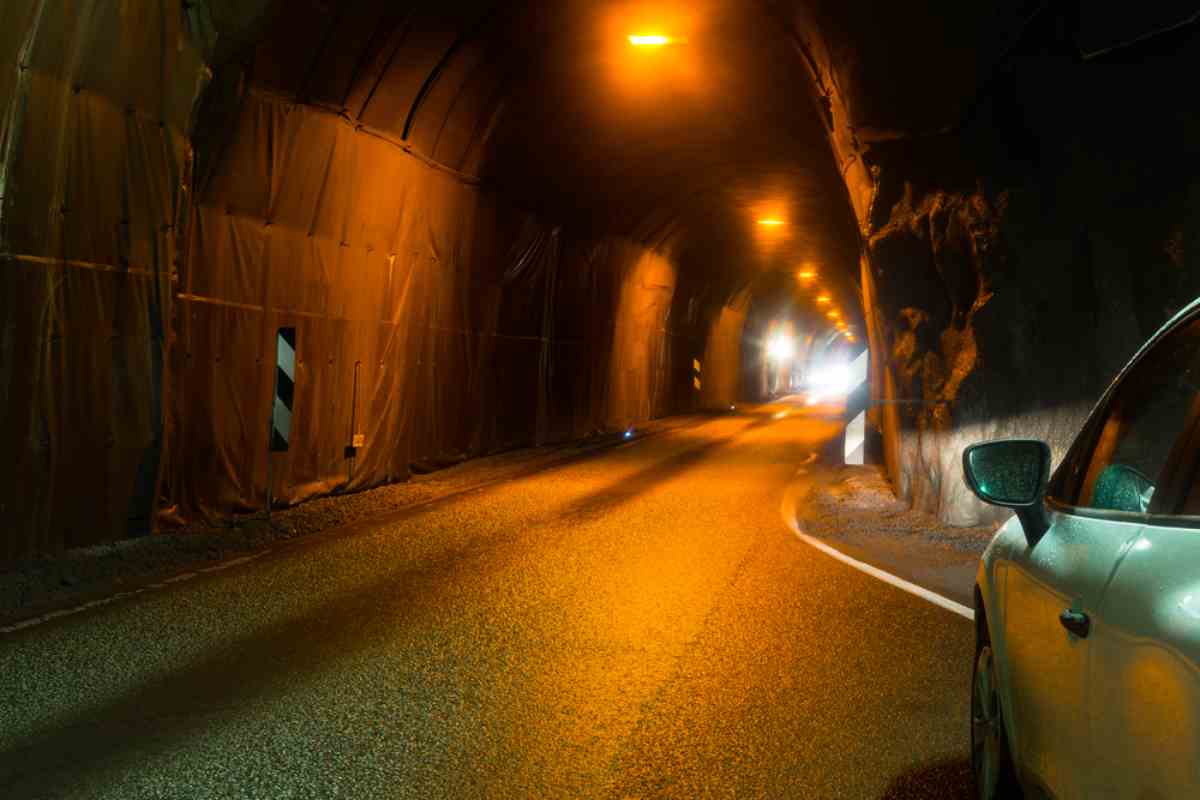 Car driving through a dim, orange-lit road tunnel in Iceland with wet pavement and rock walls.