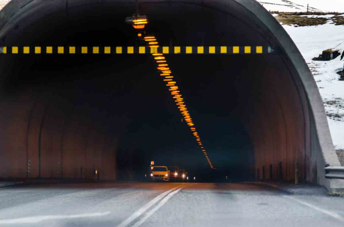 Vehicles approaching the Vaðlaheiðargöng tunnel, with overhead height markers and interior lights.