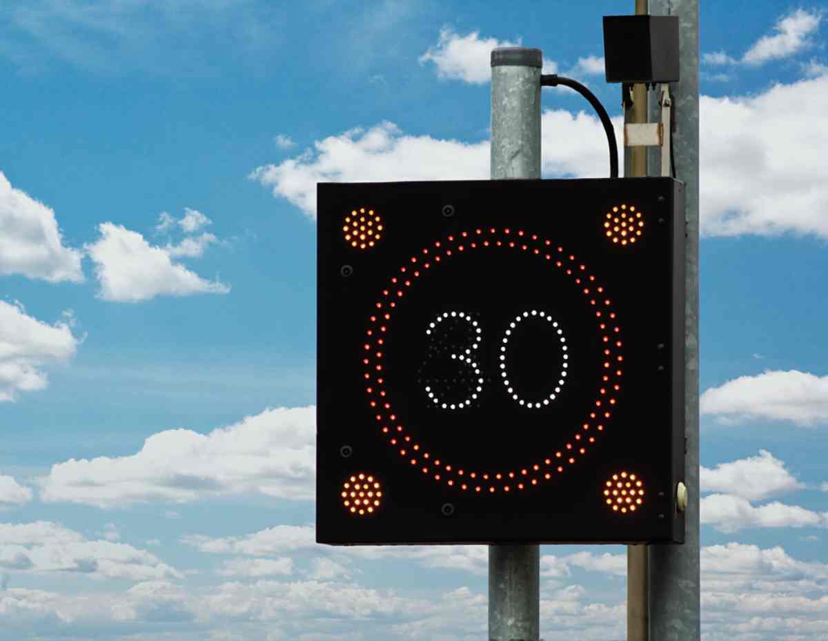 LED variable speed limit sign showing “30” against a blue sky.