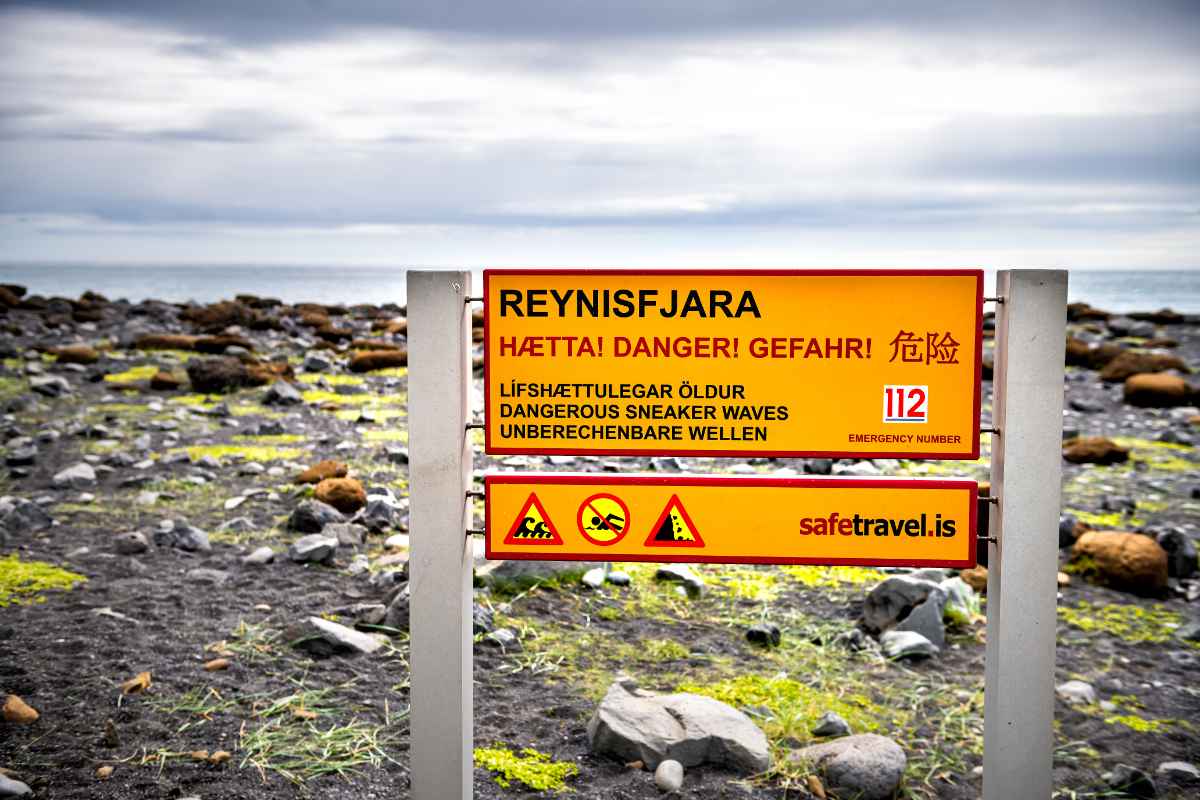 Reynisfjara warning sign about dangerous sneaker waves and hazards on Iceland’s black sand beach.