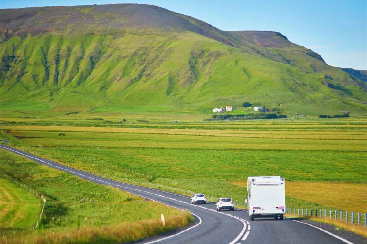 Campervan and cars on the Ring Road passing green fields and summer mountains.