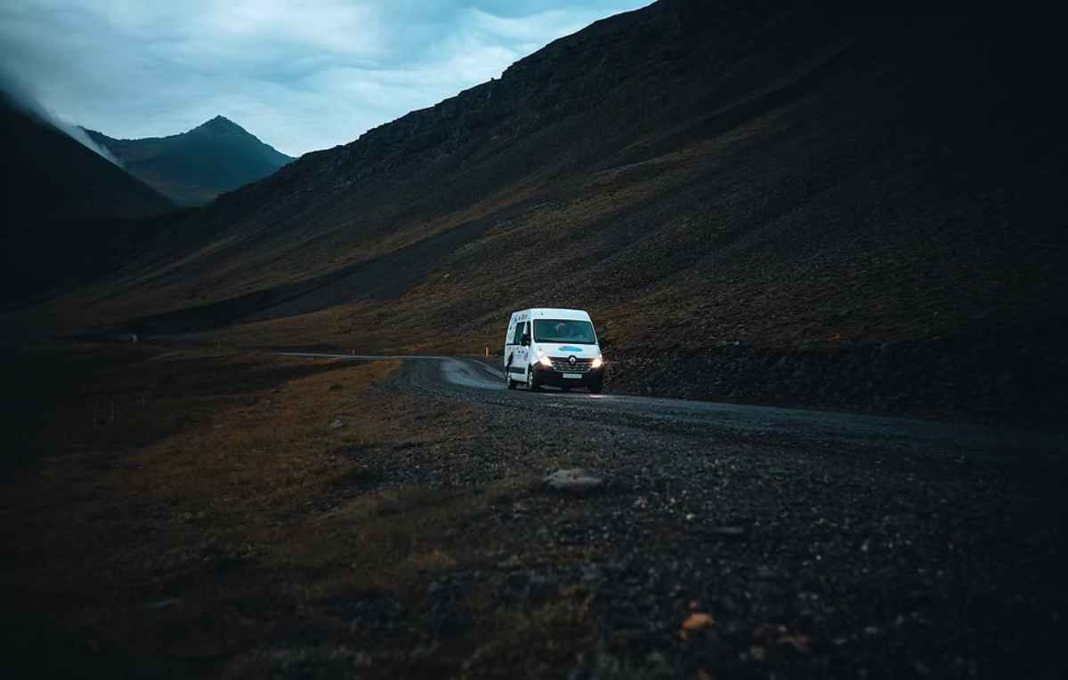 White campervan driving through a dark mountain valley on a winding Icelandic road at dusk.