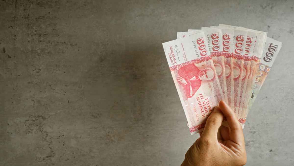 Hand fanning Icelandic kr&oacute;na banknotes against a gray concrete background.