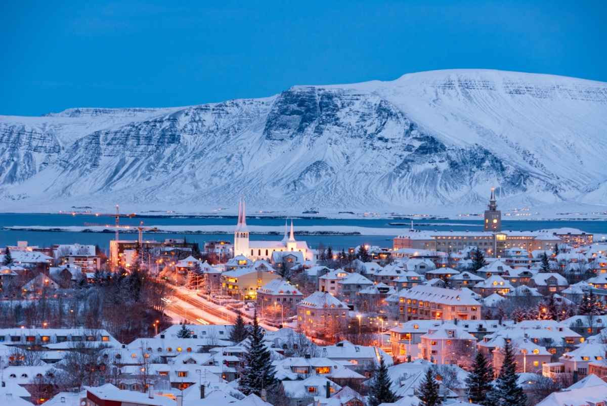 Reykjavik’s snow-covered skyline at blue hour, warm city lights glowing beneath Mount Esja and the bay.