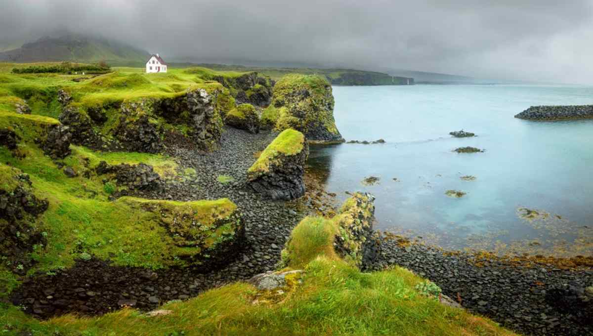 Mossy sea cliffs and a lone white house at Arnarstapi on the Sn&aelig;fellsnes coast.
