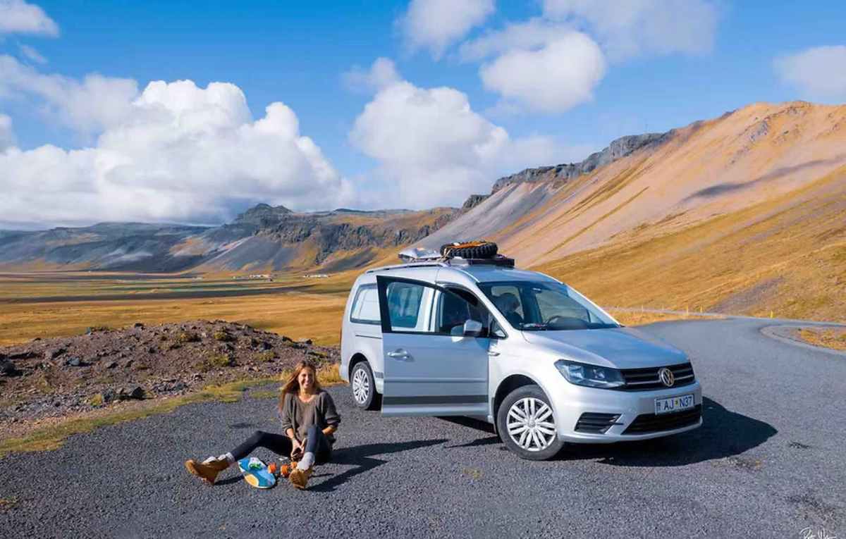 Traveler picnicking next to a compact camper car on a scenic mountain road with wide open views.