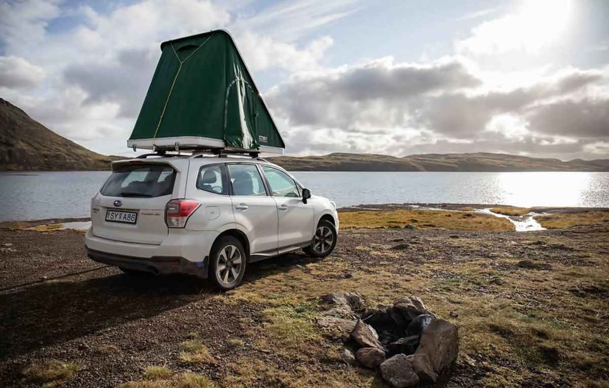 SUV with a rooftop tent set up beside a calm Icelandic lake under bright afternoon sun.