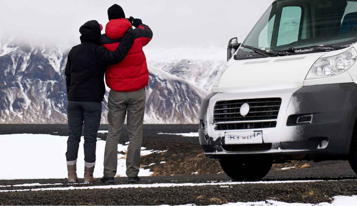 Couple enjoying the view in Iceland during Winter next to their parked rental campervan