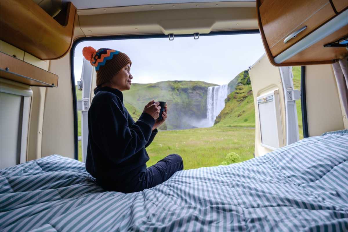 Tourist drinking a cup of coffee by Skogafoss from her campervan