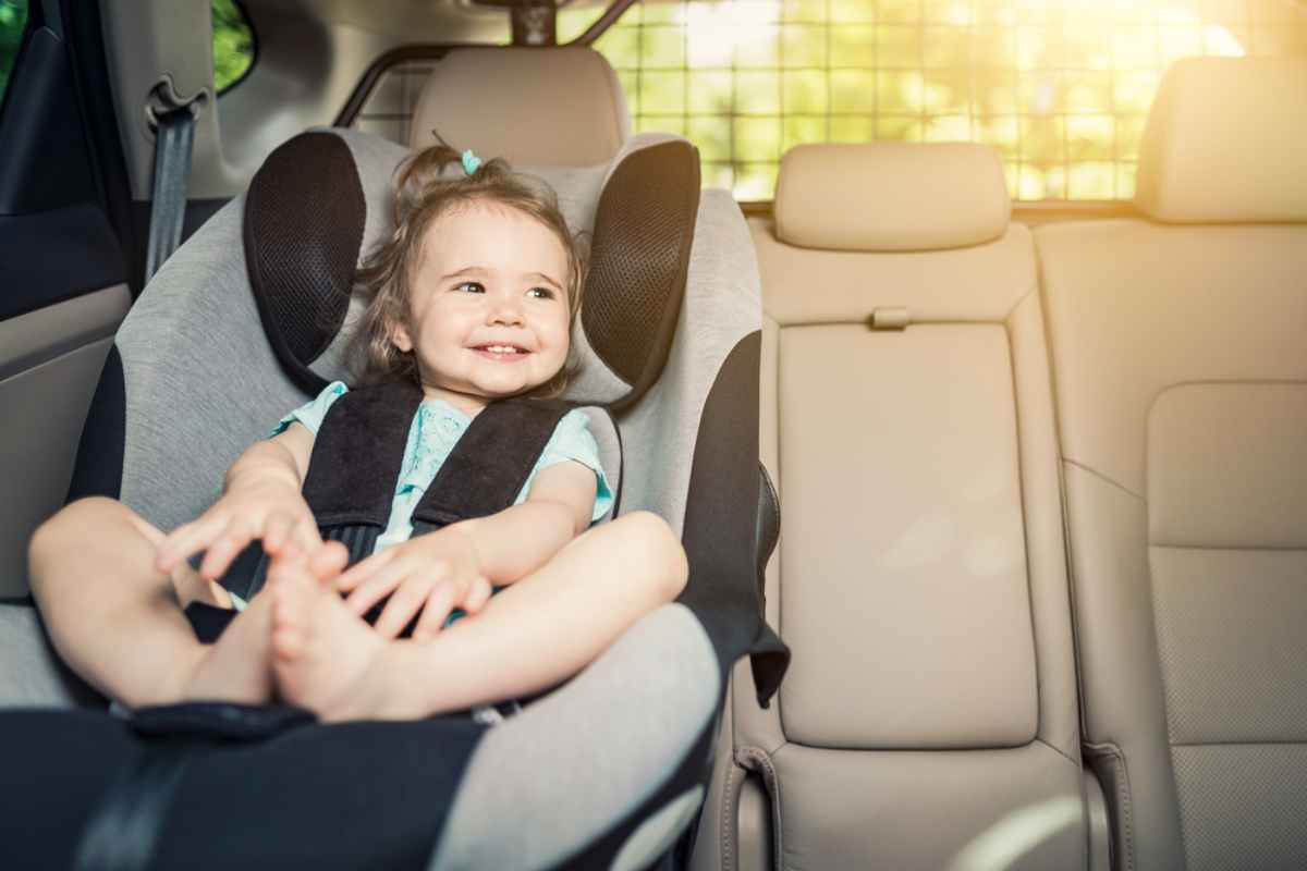 Smiling toddler in a car seat, relaxed, with sunlight streaming in. Beige car interior, joyful mood.