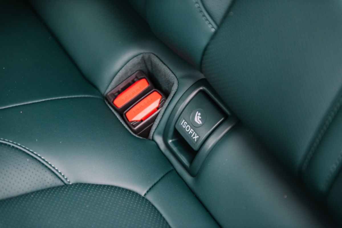 Close-up of a car's green leather seat with red seatbelt buckles and an ISOFIX label.